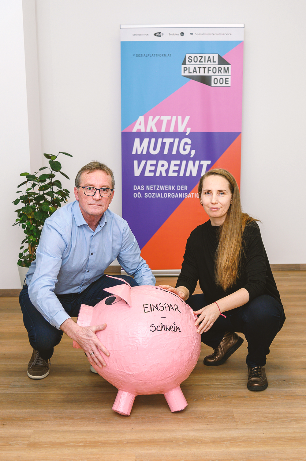 Josef Pürmayr und Manuela Hiesmair halten ein übergroßes Sparschein aus Papiermache, auf dem Einsparschwein steht.