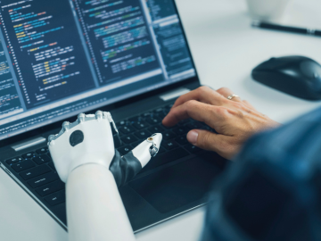Man sieht einen Mann am PC arbeiten, der einen robotischen Arm hat.