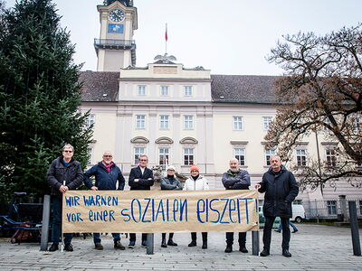 Sieben Menschen stehen mit einem Transparent vor dem Landhaus.