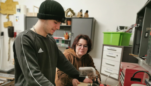 Eine Frau unterstützt einen jungen Burschen bei der Arbeit an einer Maschine